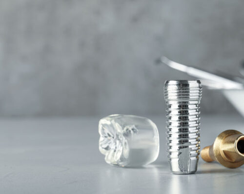 Dental implant pieces laying on a on a table, close up image of dental implant model. Reflecting off of the gloss table it shows all parts of a dental implants