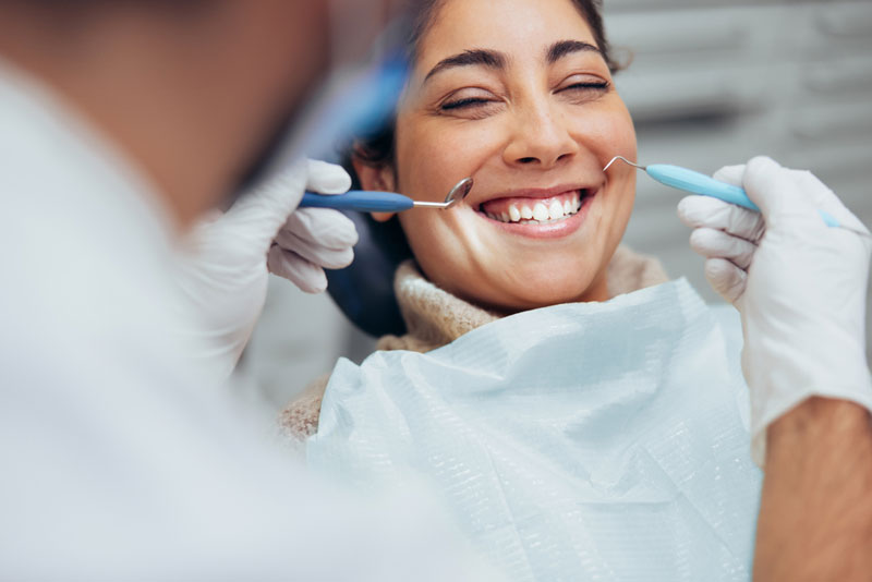 Dentist performing professional teeth cleaning on a smiling female patient using a dental handpiece during a routine dental visit."